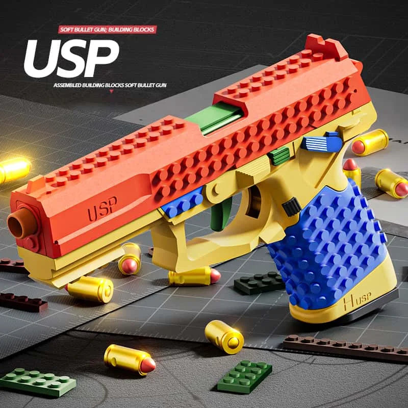 An assembled building block soft bullet gun toy in orange and yellow, shown on a gray surface with loose blocks.