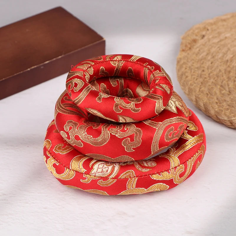 Handmade red singing bowl cushion with gold embroidery resting on a light surface.