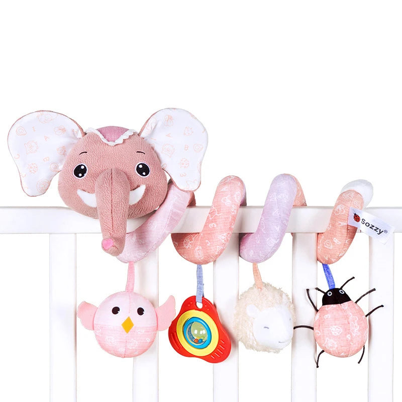 A plush elephant sensory toy with pink ears and a pink trunk hanging from a white wooden crib railing.