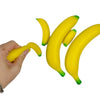 A hand is holding a bright yellow banana stress relief toy with green tips.