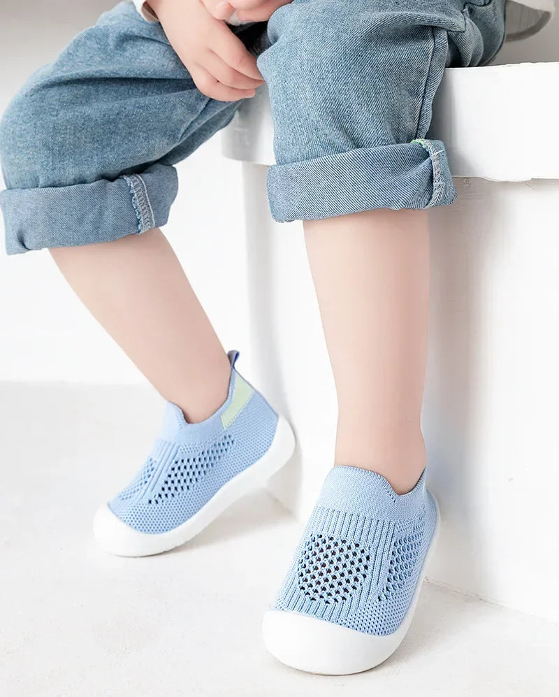 A pair of light blue breathable mesh slip-on sneakers for toddlers resting on a white surface.