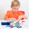 A young boy is sorting wooden shape puzzle pieces like rings and cutouts on a white table.