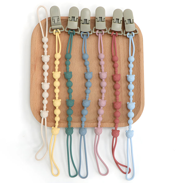 A collection of silicone pacifier clips in various pastel colors attached to a wooden board.