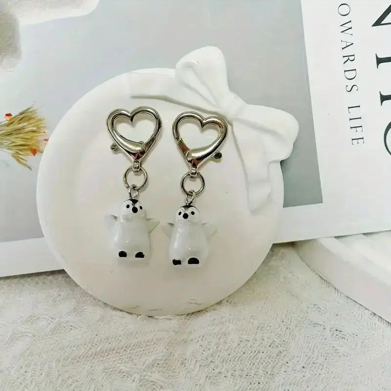 A set of two silver heart-shaped keychains featuring cute white penguin charms on a white ceramic dish.