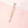 A gold and silver refillable diamond picking pen with a rotating wax tip resting on a pink surface.