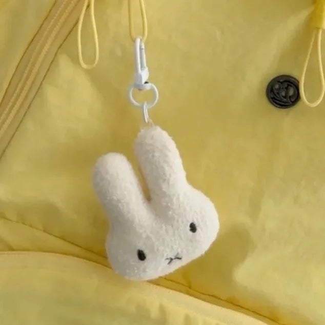 A white Miffy cartoon rabbit keychain pendant hanging from a yellow fabric.