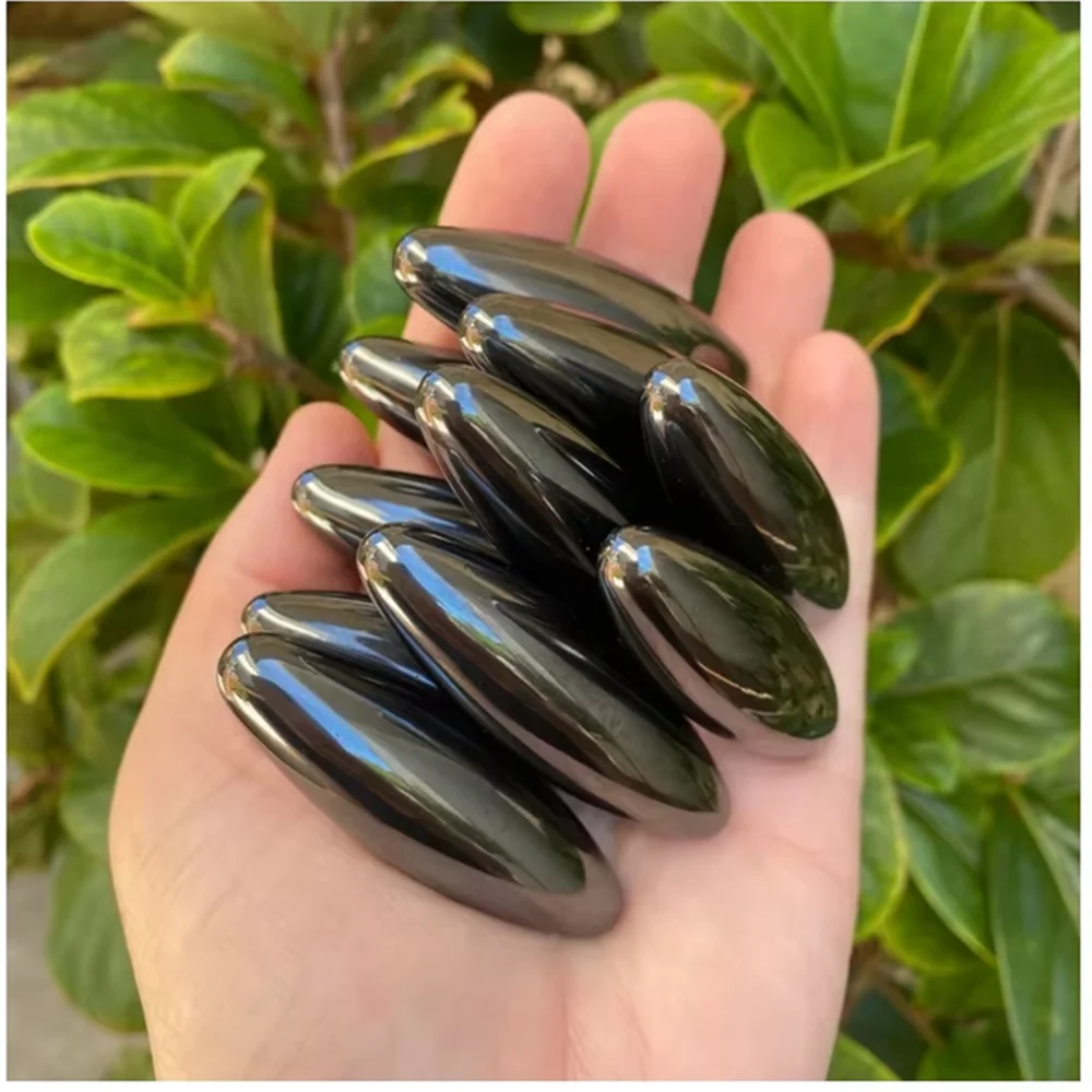 A hand holds several smooth, dark olive green magnetic snake egg fidget toys against a blurred green leaf background.