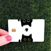 A white card featuring black cat face stickers with glowing yellow eyes on a green grass background.