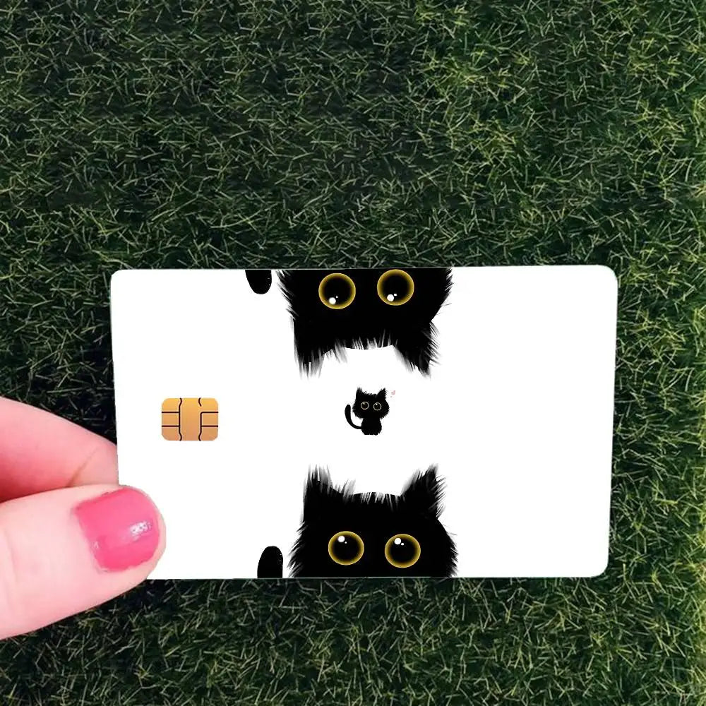 A white card featuring black cat face stickers with glowing yellow eyes on a green grass background.
