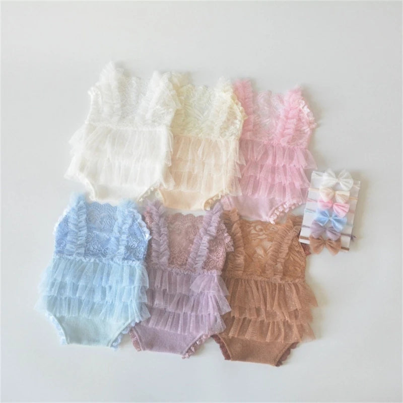 A collection of sheer lace baby rompers in pastel shades including white, cream, pink, and blue, laid out on a white surface.