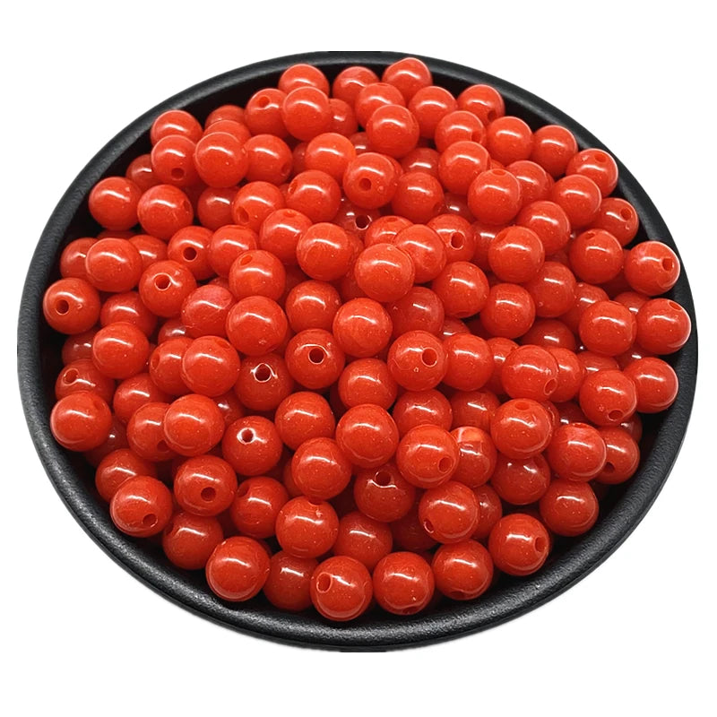 A pile of bright orange acrylic round beads for jewelry making in various sizes.