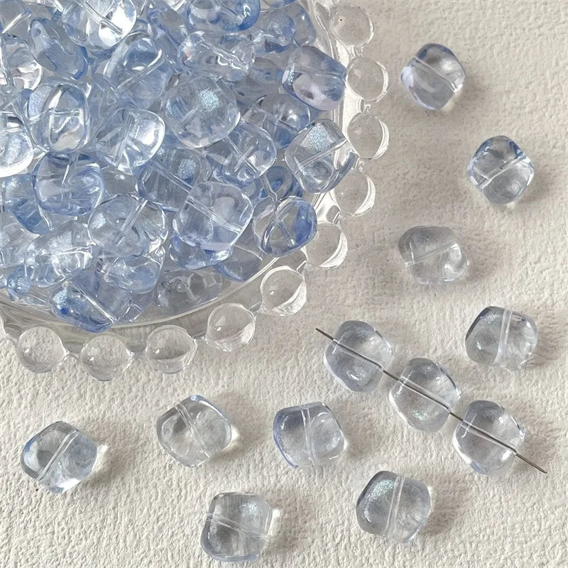 A pile of irregular square geometric glass beads for jewelry making on a light surface.