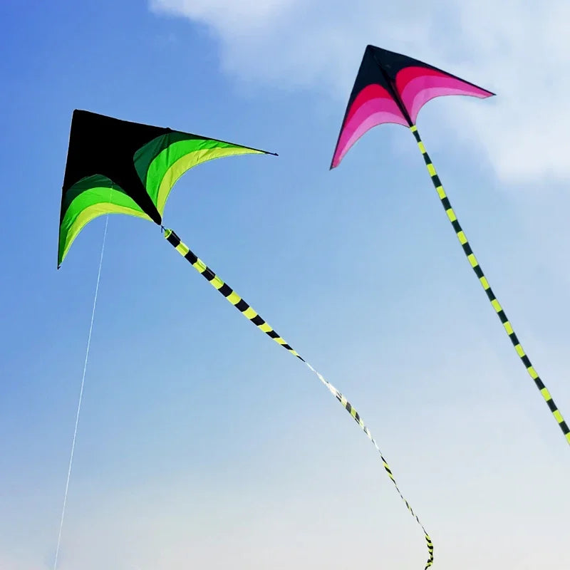 A large delta kite with a black and green canopy and a yellow and black striped tail flying against a blue sky.