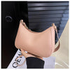 A light pink PU square crossbody bag with a zipper closure being held by a hand against a dark background.