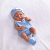 A lifelike vinyl reborn doll with a blue outfit and matching hat lying on a white surface.