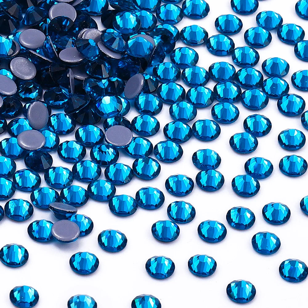 A close-up view of various blue glass crystal hot fix rhinestones scattered on a white background.