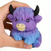 A purple and blue Scottish Highland cow stress relief squishy toy is held in a hand.