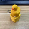 A yellow duck fidget clicker keychain with a silver ring and LED light resting on a wooden surface.
