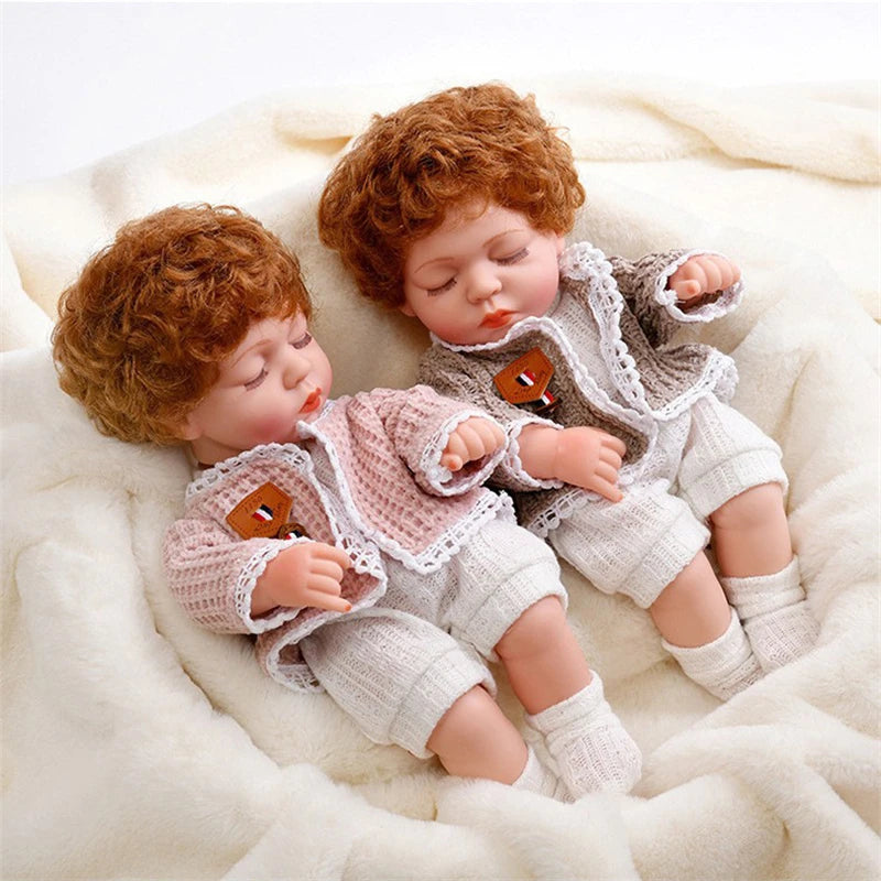 Two realistic 12-inch reborn dolls with curly red hair wearing matching cozy winter rompers on a white fluffy blanket