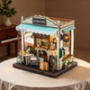 A detailed wooden dollhouse kit of a coffee shop featuring an awning and display window.