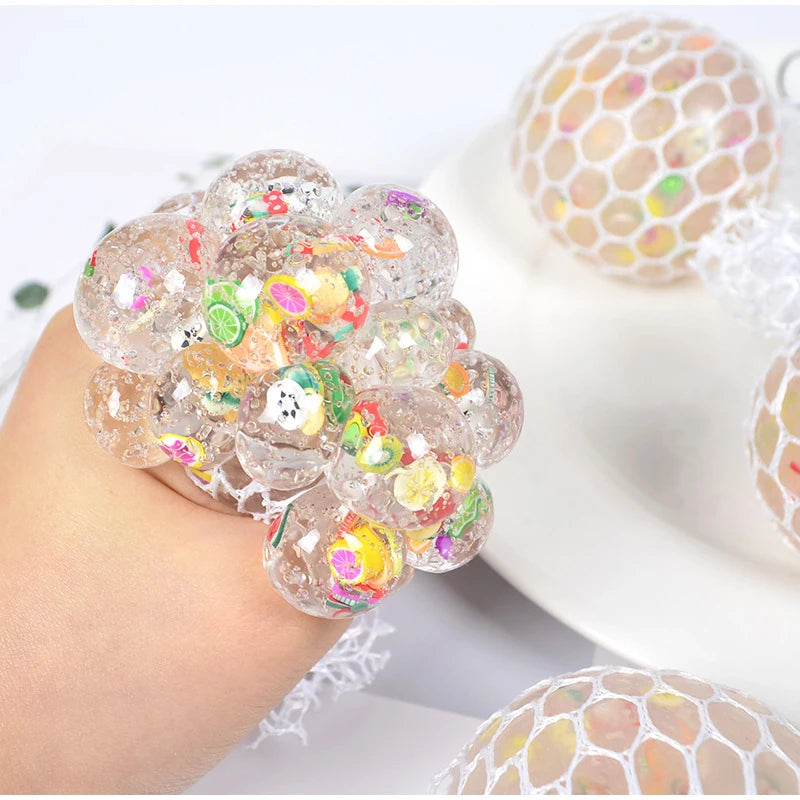 A hand holds a cluster of colorful, translucent stress relief balls with mesh netting on a white background.