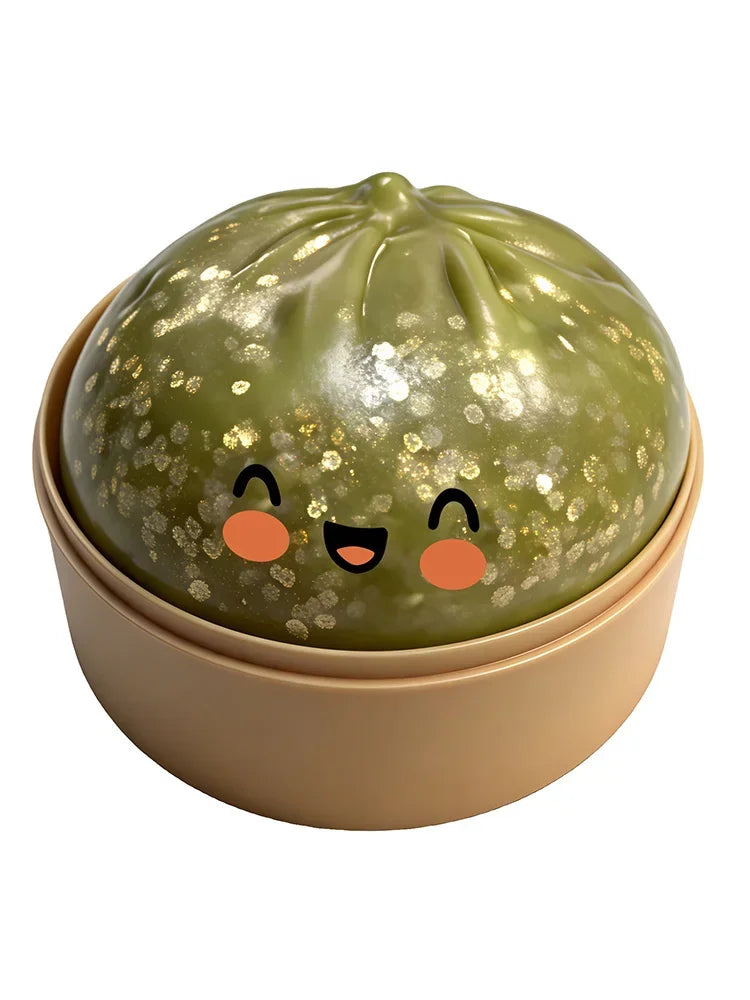 A round, olive green squishy toy shaped like a dumpling with gold glitter speckles and simple black eyes.