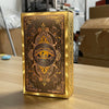 A rectangular box of golden foil tarot cards featuring an ornate eye design and decorative patterns.
