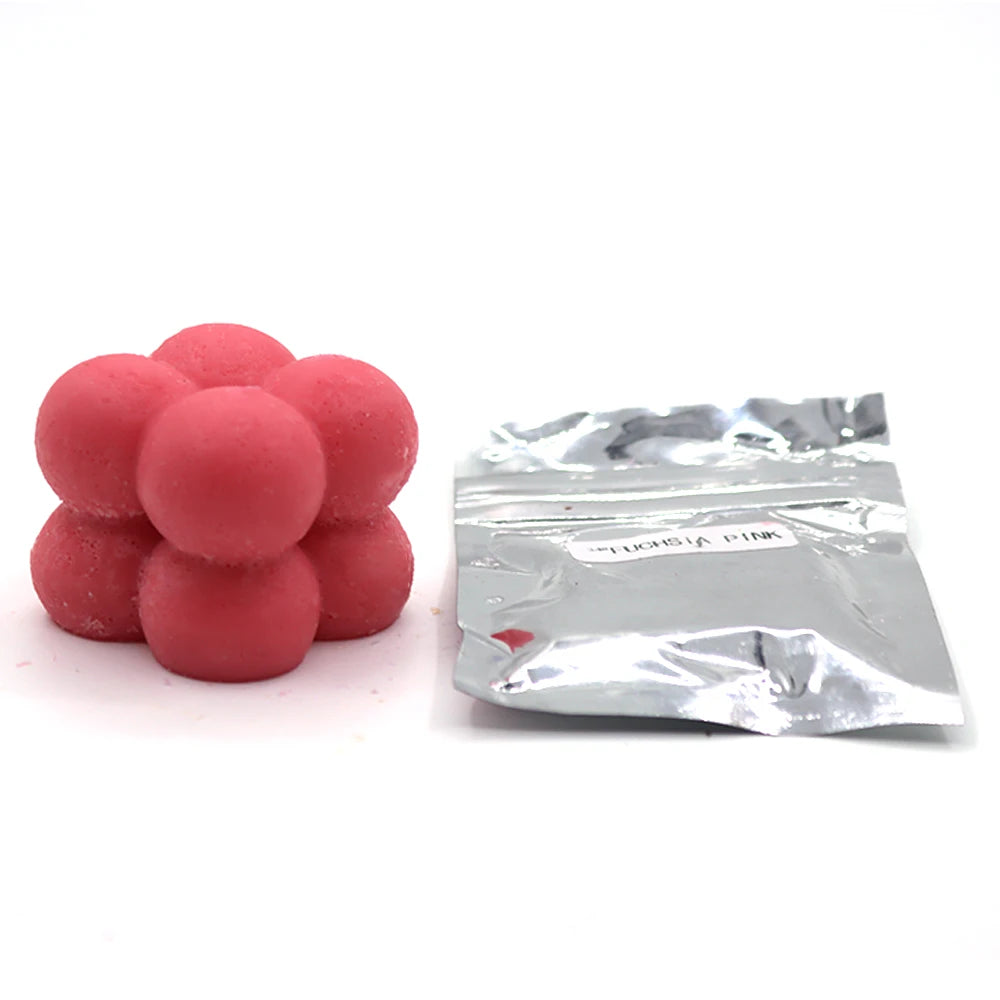 A pile of pink candle dye chips next to a small silver foil packet.