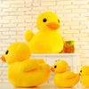 A bright yellow plush toy of a duck sitting on a white shelf against a brick background.