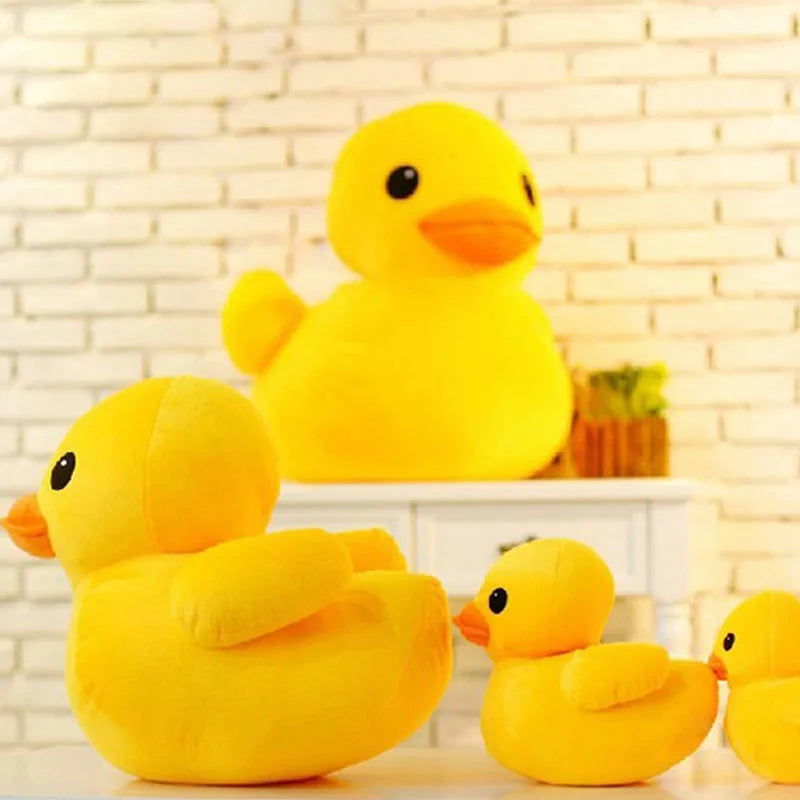 A bright yellow plush toy of a duck sitting on a white shelf against a brick background.