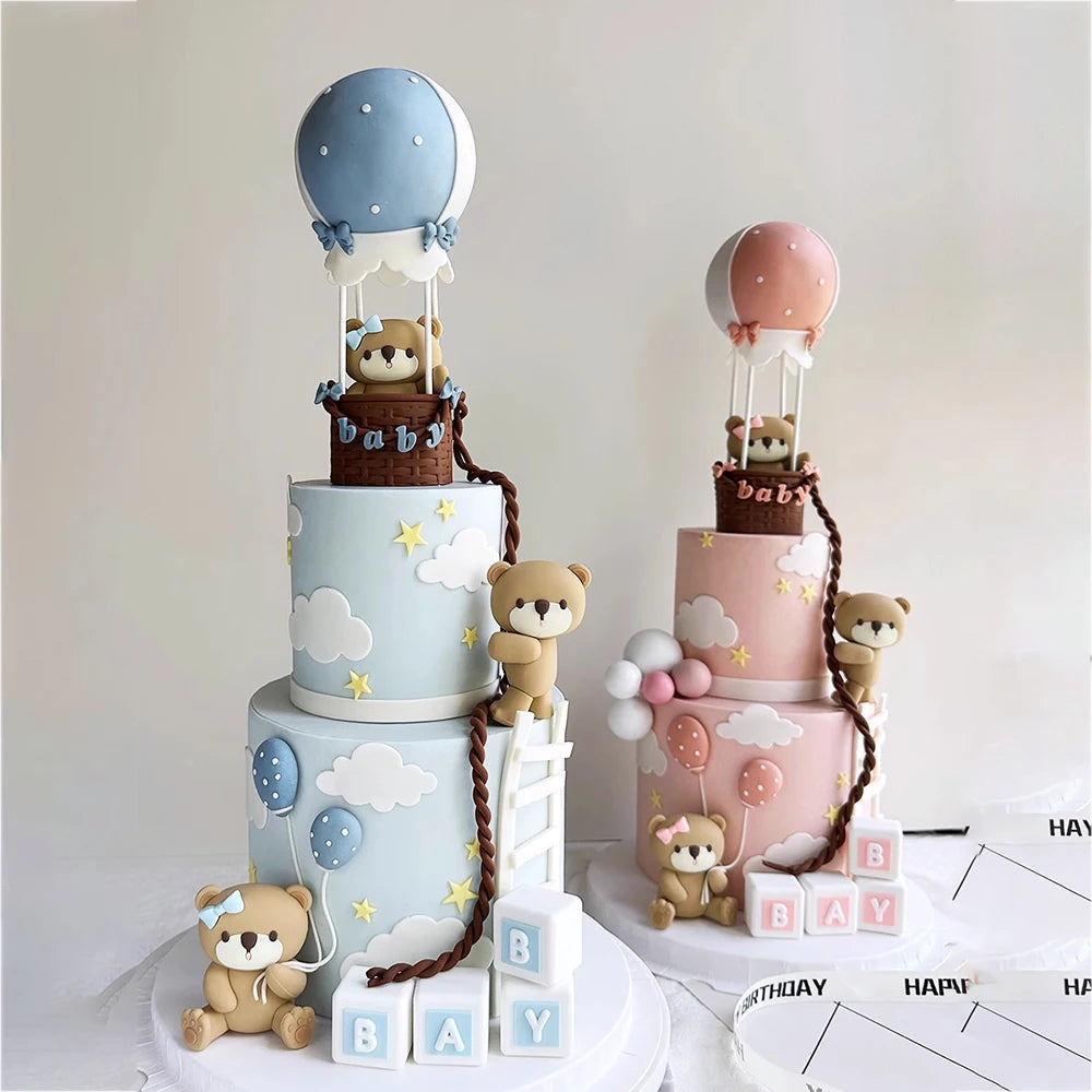 A tiered cake display featuring blue and pink fondant elements, including bear figures and clouds.