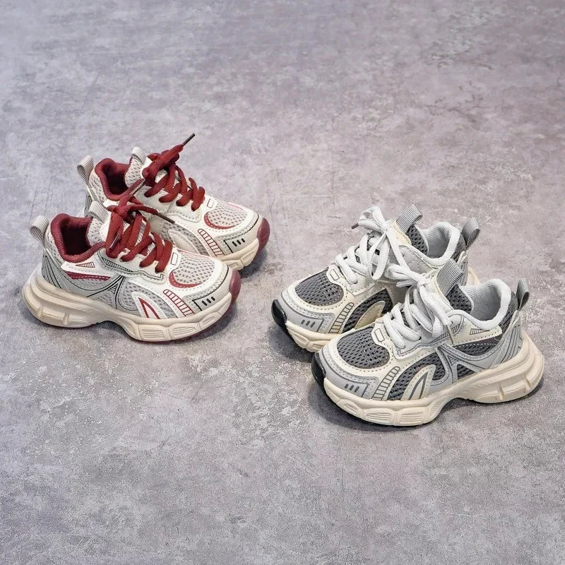 A pair of red and white breathable mesh kids running sneakers with cushioned soles resting on a gray surface.