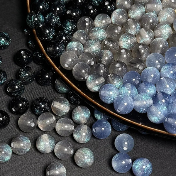 A close-up of various iridescent and glittery resin beads in black, silver, and blue shades.