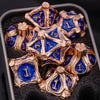 A set of seven gold and blue metal dice for tabletop role-playing games displayed in a dark box.