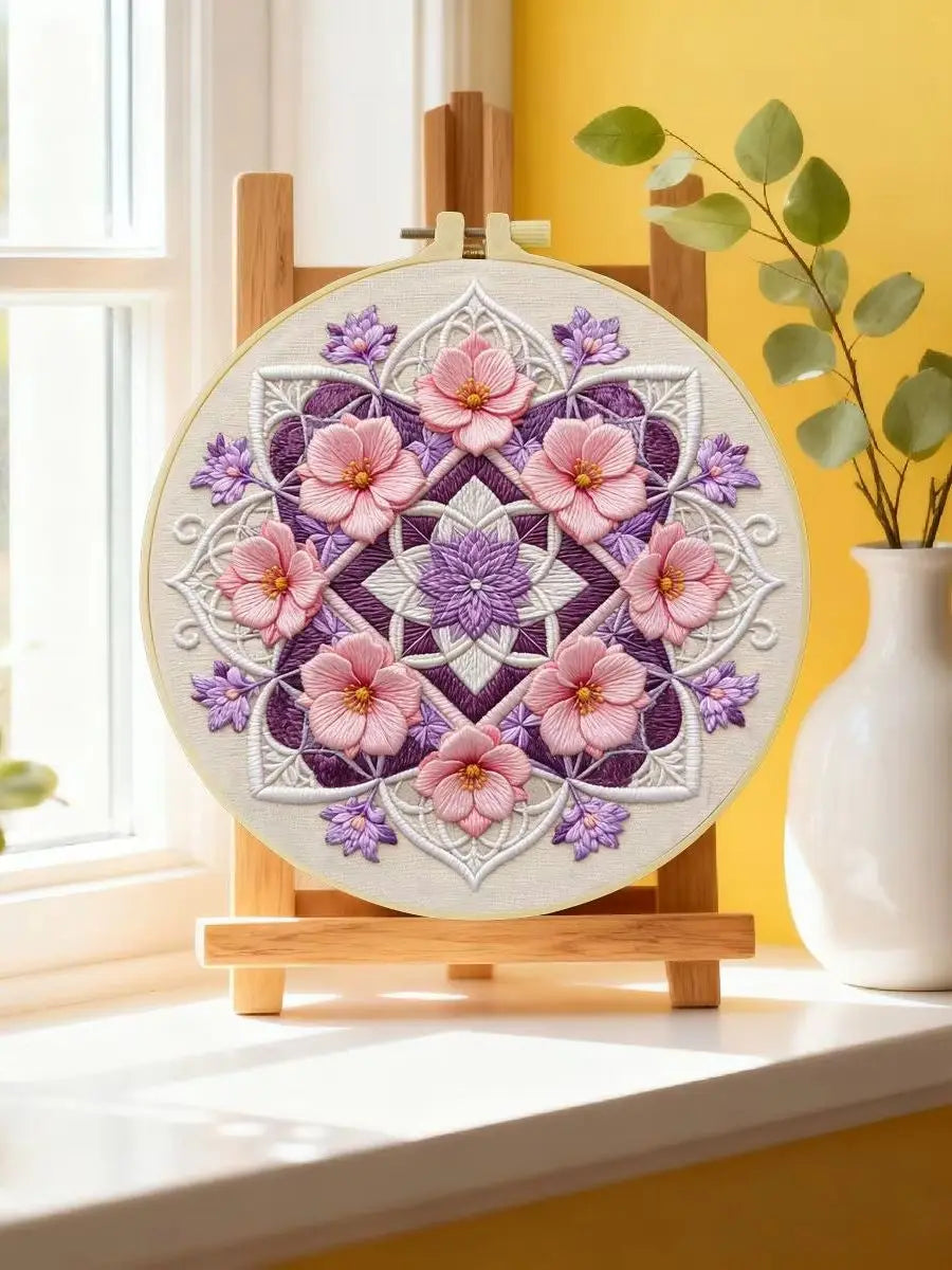 A circular flower embroidery design featuring pink and purple flowers on a beige fabric, displayed on a wooden easel.