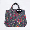 A black fabric tote bag featuring a playful pattern of pink and yellow dots and red striped accents, with a black plush hippo