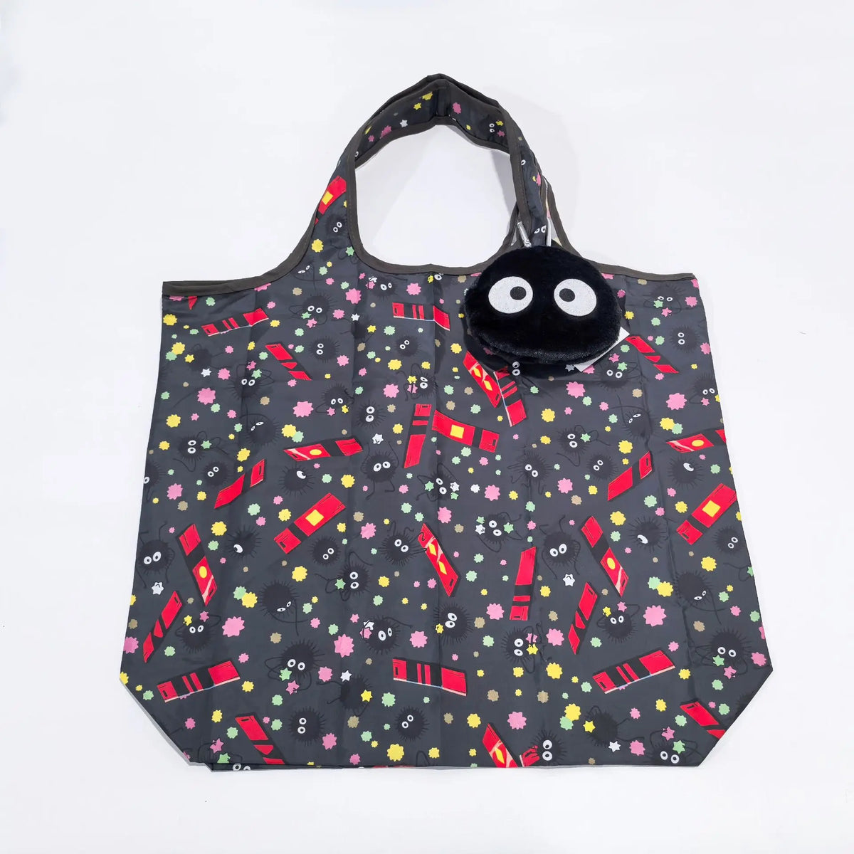 A black fabric tote bag featuring a playful pattern of pink and yellow dots and red striped accents, with a black plush hippo