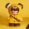 A yellow plush doll with brown fur and a hood, featuring a small camera pendant.