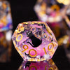A close-up of a translucent purple polyhedral die with a black cat design and gold numbers, reflecting on a dark surface.