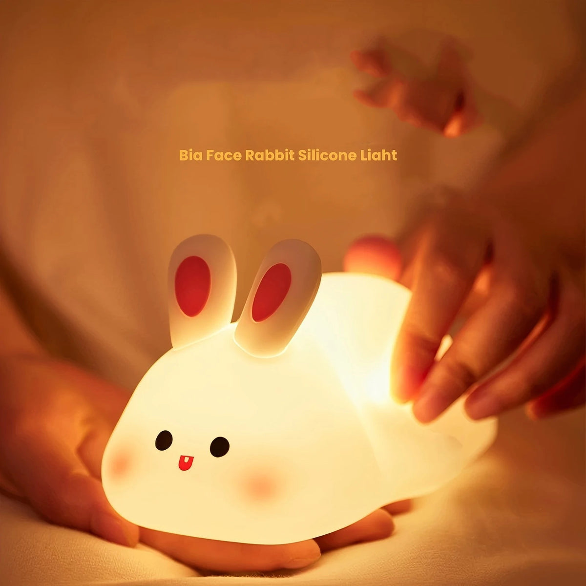 A glowing white silicone rabbit night light is held in a person's hand against a soft background.