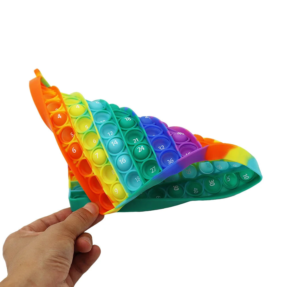 A hand holds a colorful multiplication pop-it fidget toy with numbered silicone bubbles.