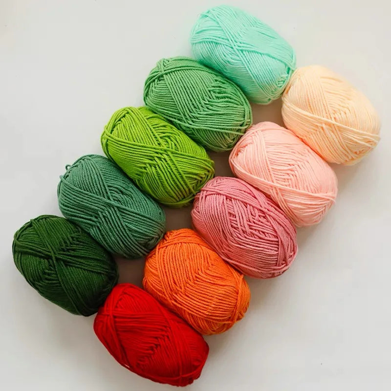 A collection of pre-dyed milk cotton yarn in various shades of green, pink, and orange scattered on a white surface.