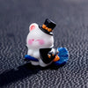 A white cartoon bear figurine wearing a black top hat and blue accents, displayed on a dark surface.