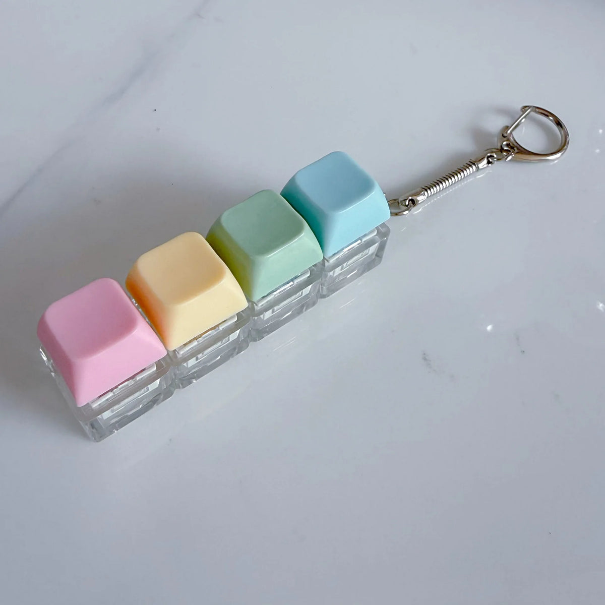 A keychain featuring five pastel colored, square fidget toys attached to a silver chain.