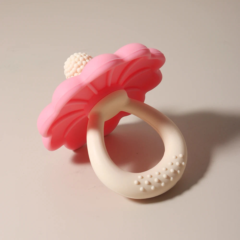Rosa Silikonblume und Schnuller-Teether mit einer weißen Kugel auf hellem Hintergrund