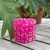 A stack of 36 transparent pink dice in a clear display case resting on a wooden surface.