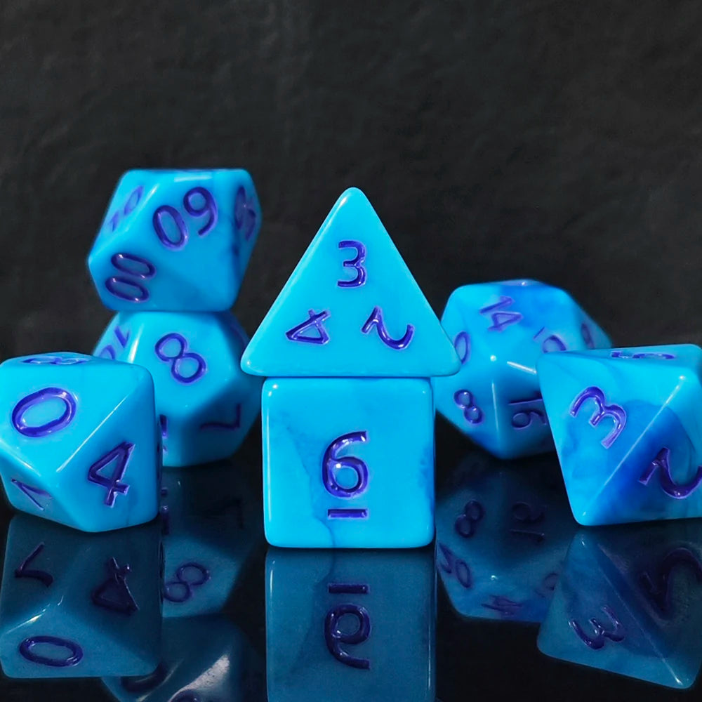 A collection of seven polyhedral dice in shades of blue and purple are displayed on a reflective surface.