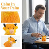 A man is gently touching a small, orange glitter highland cow squishy stress relief toy.