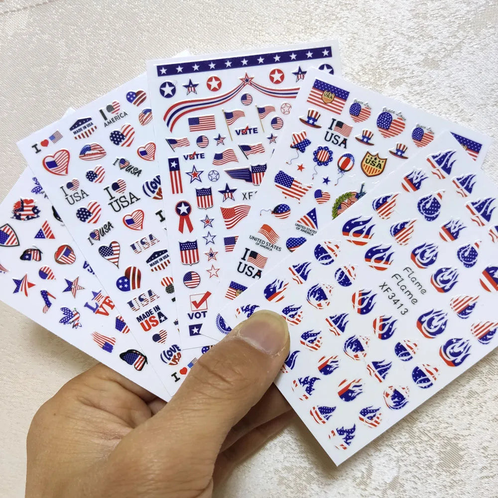 A hand holds a fan of USA flag nail decals for DIY decoration featuring various patriotic designs and stars.