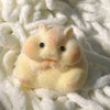A small, yellow silicone hamster fidget toy is nestled in white fluffy material.